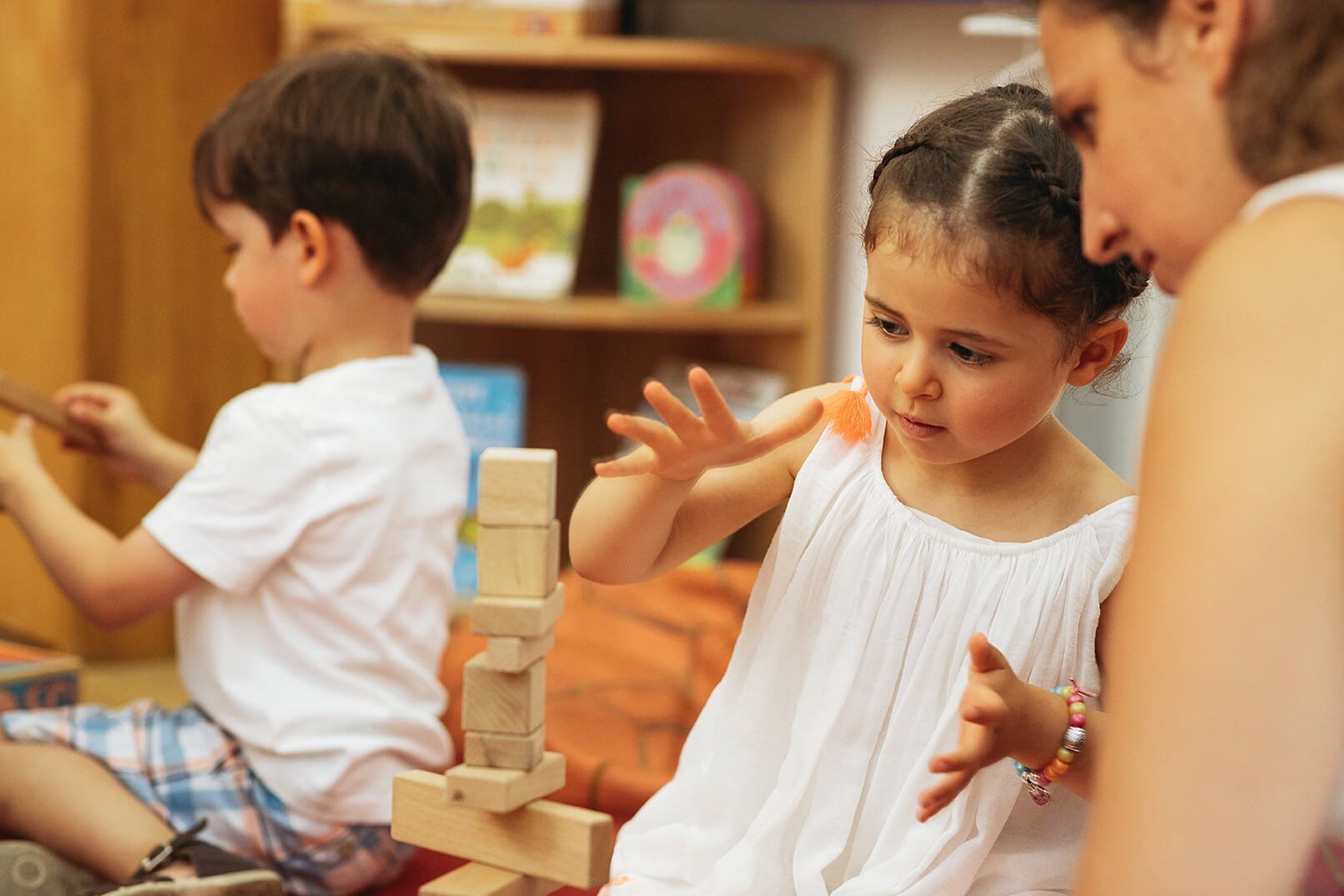 A girl balancing wooden blocks into a tower beside her teacher