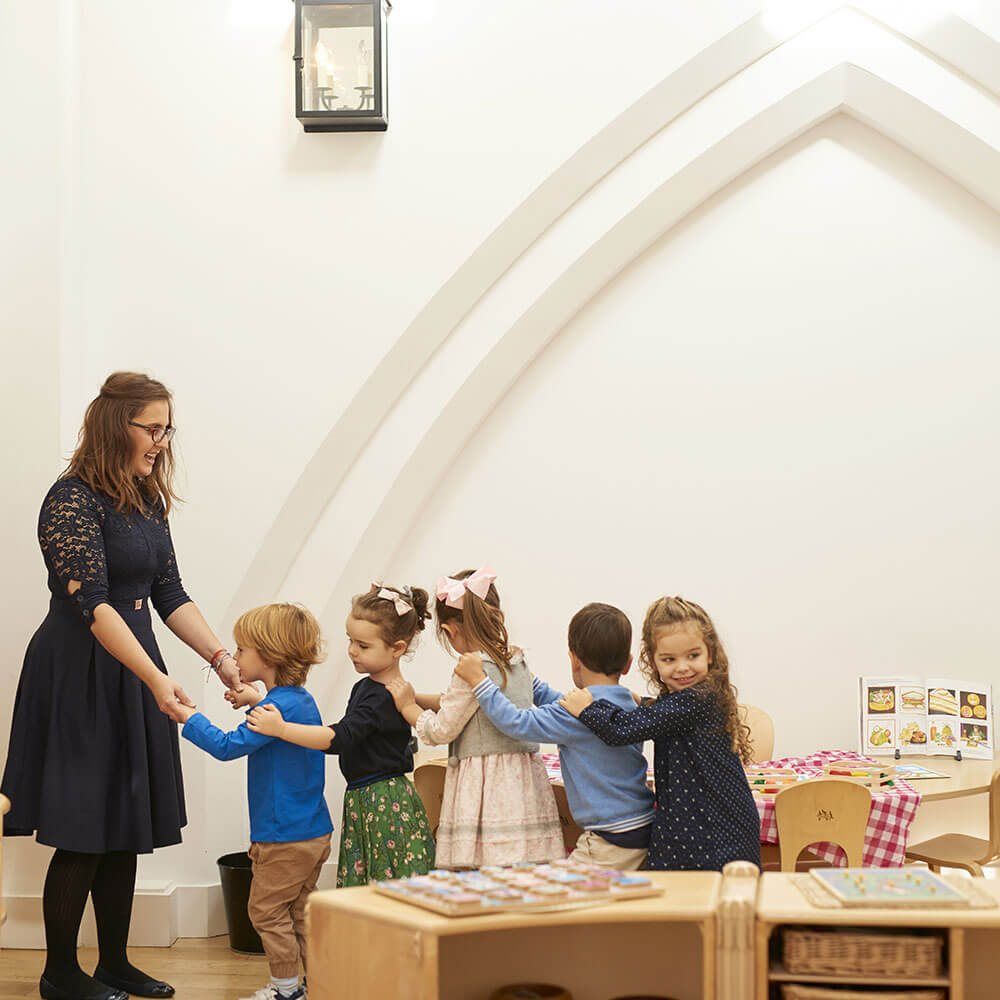 A teacher and children holding hands in a ring beneath a pointed archway