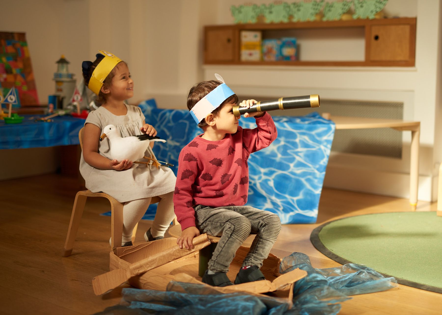 Two children playing at sailing, one holding a toy seagull and the other looking through a telescope