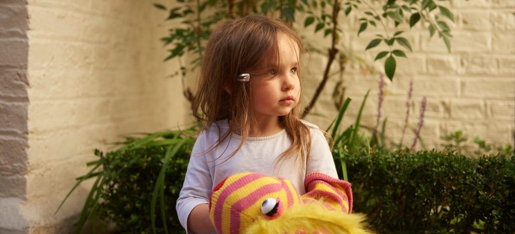 A girl in the garden holding a striped puppet