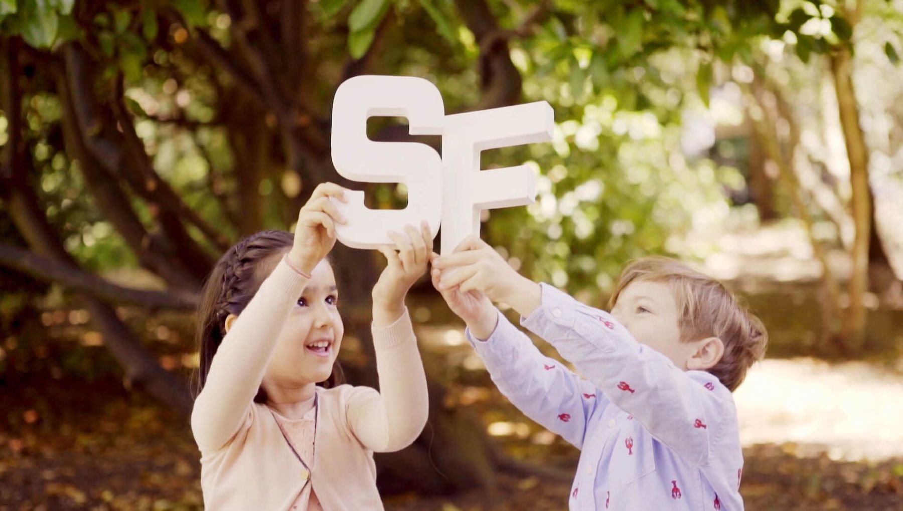 Two children in the garden holding up large white letters S and F