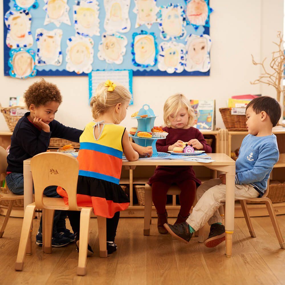 Children at a classroom table beneath a wall of their own portraits