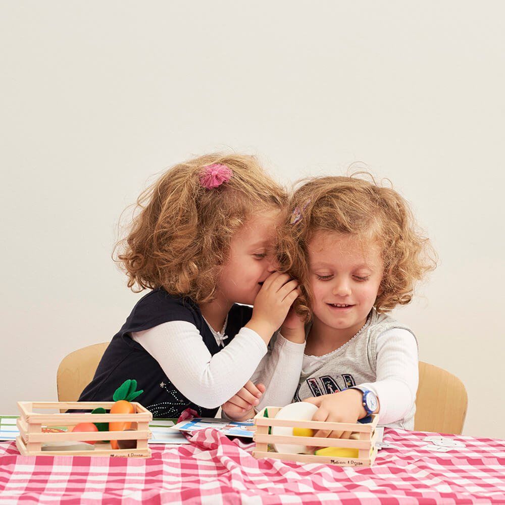 One girl whispering to another at a table laid with a pink gingham cloth