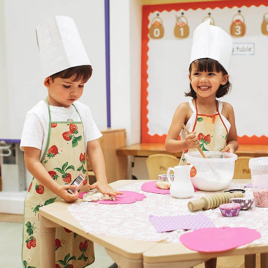 Two children in chef hats and strawberry aprons baking